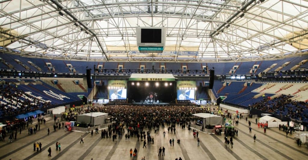 A wide shot of a large indoor arena with a stage set up in the distance and a large crowd of people on the floor.