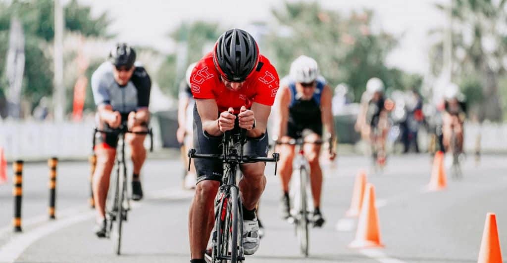 A group of cyclists are riding in a race on a road, wearing helmets and racing gear.
