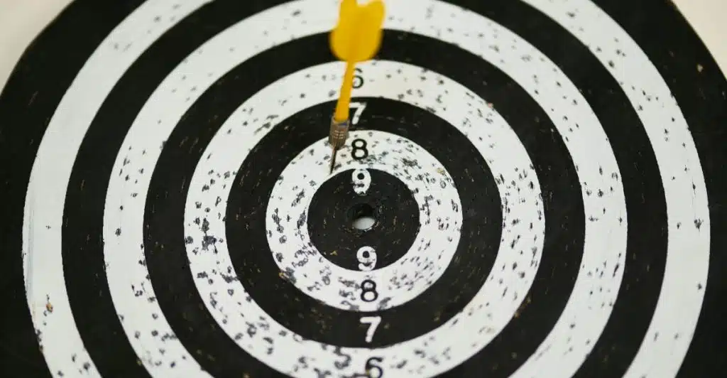 A close-up shot of a yellow dart hitting near the bullseye of a black and white target.