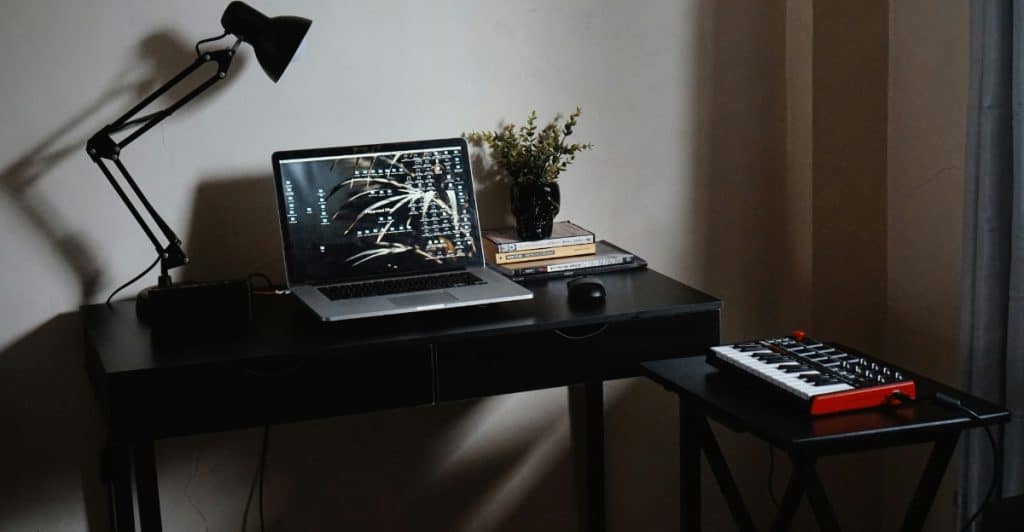 A black desk with a laptop, plant, books, and a musical keyboard.