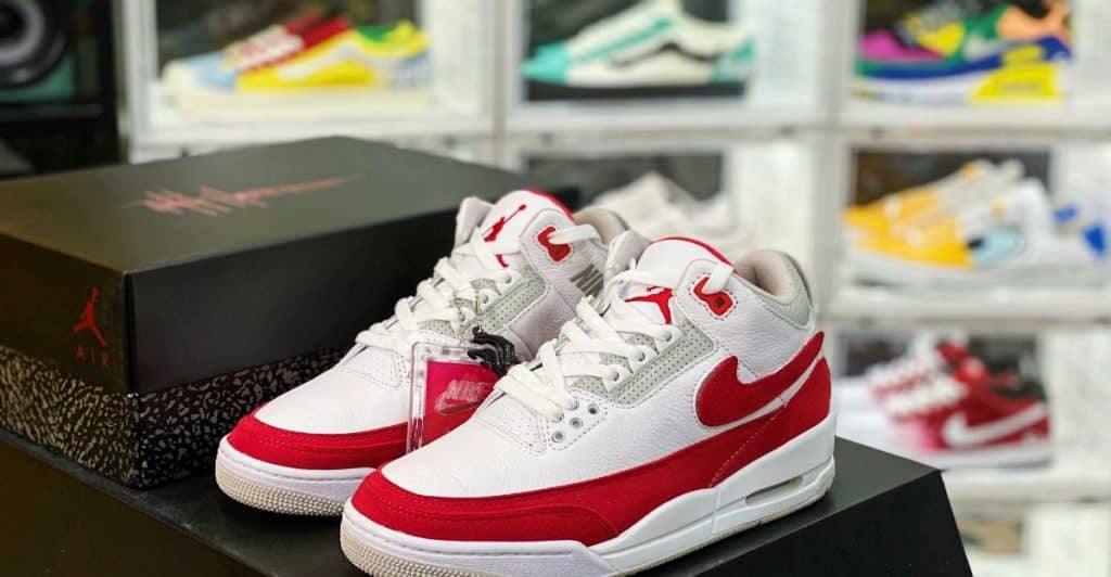 A pair of white and red sneakers in the foreground with a display of various sneakers in clear boxes in the background.