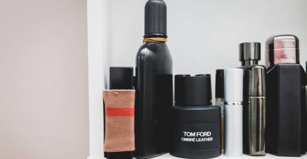Bottles of men's colognes arranged on a white shelf, including a large black cylindrical bottle and a black Tom Ford bottle.