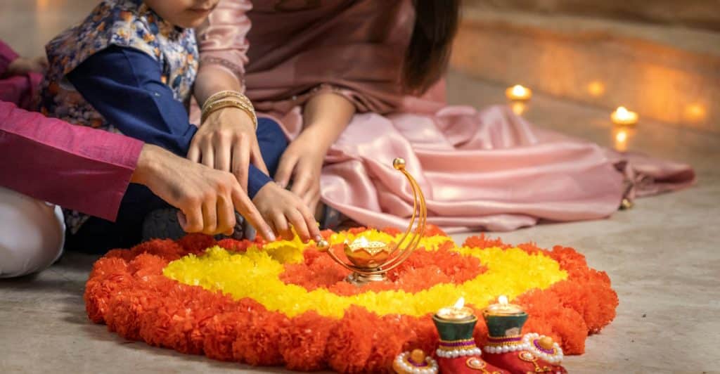 Family members arranging a flower decoration and lighting candles for Diwali.