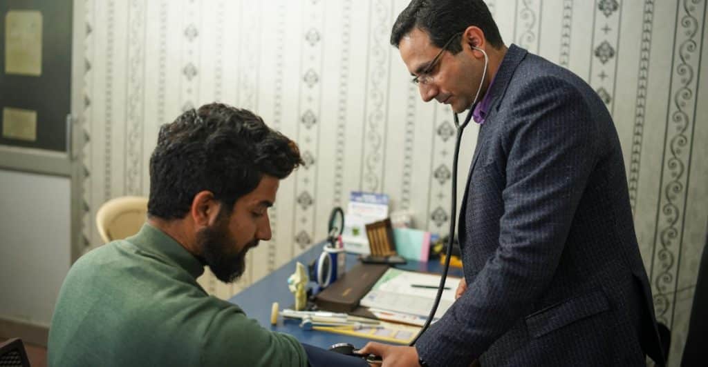 A doctor with a stethoscope examining a seated male patient.