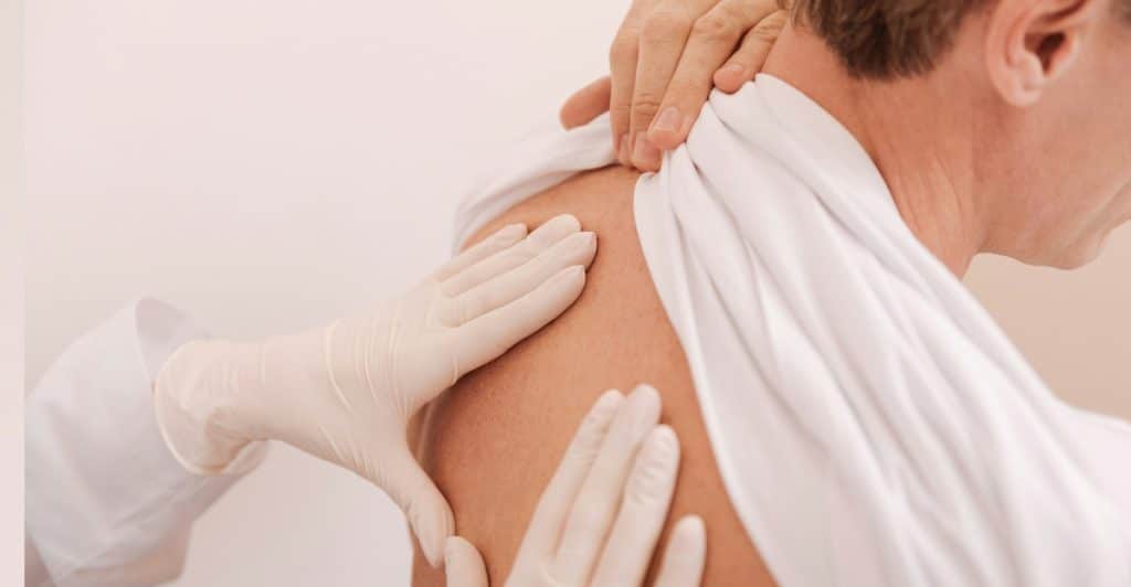 A doctor wearing gloves examining a person's upper back.