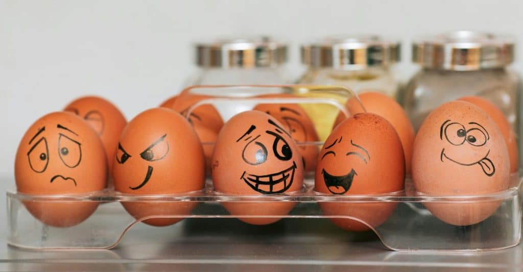 A carton of brown eggs with various hand-drawn faces depicting different emotions.