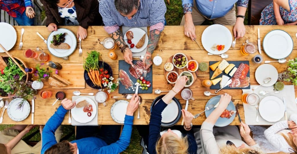 A group of people seated around a long wooden table, sharing a meal outdoors.