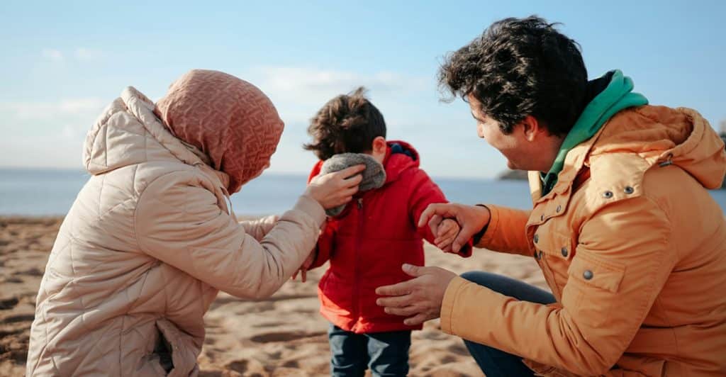 A family of three on a beach, with the parents attending to a child.