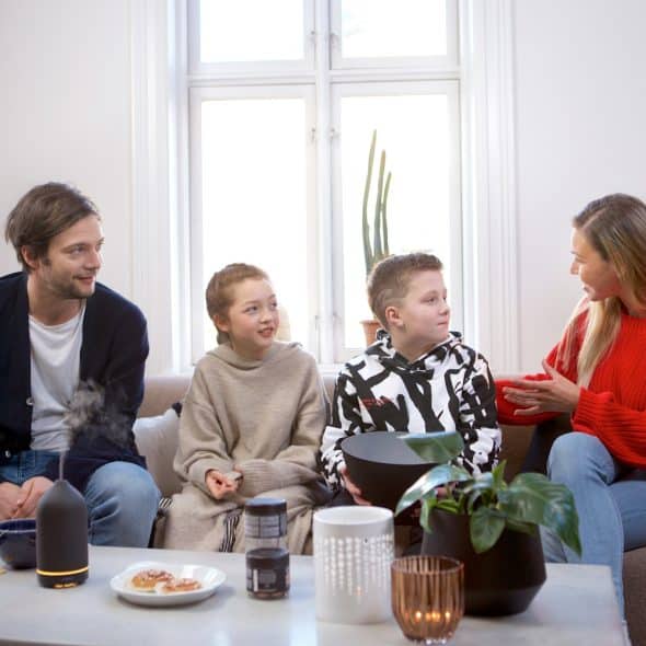A family of four is sitting on a couch in a living room, engaged in a conversation.