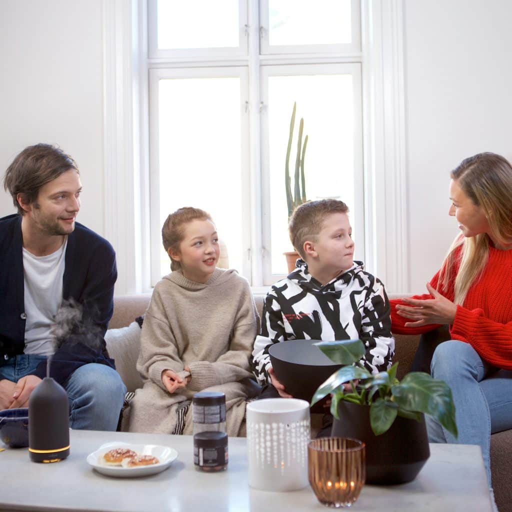 A family of four is sitting on a couch in a living room, engaged in a conversation.
