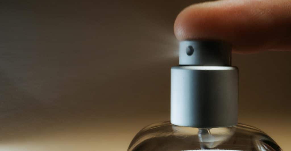 A close-up of a finger pressing the spray nozzle of a perfume bottle.