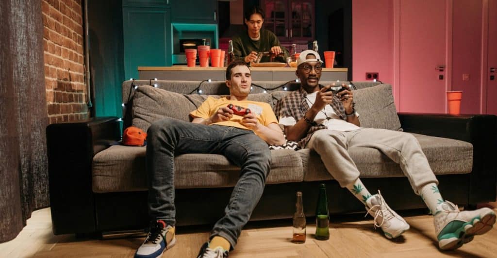 Two men playing video games on a couch while another person is in the background, illustrating maintaining independence and having fun.