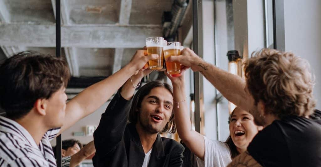 A group of friends raising their beer glasses for a toast in a lively indoor setting.