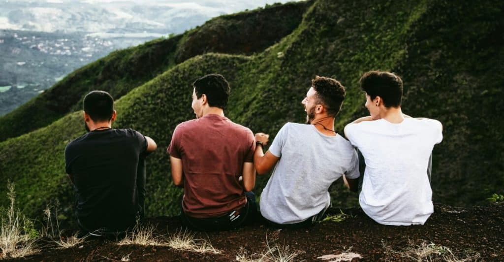 Four people sitting on a rocky outcrop overlooking a mountainous view.
