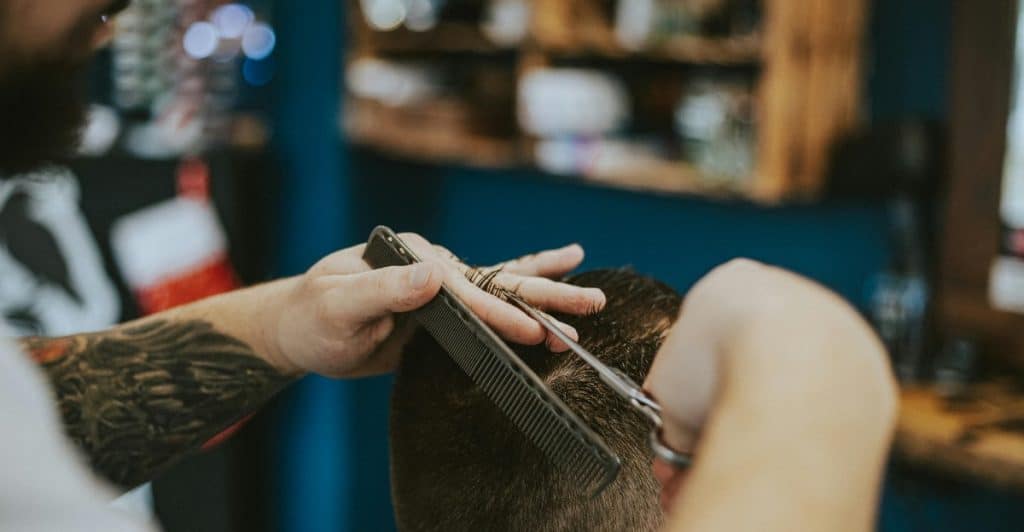 A barber is giving a haircut to a person, using scissors and a comb.
