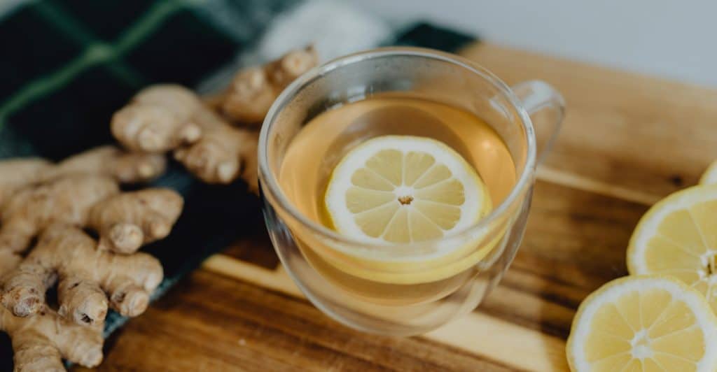 Ginger root and sliced lemons next to a clear glass mug with a lemon slice in it.
