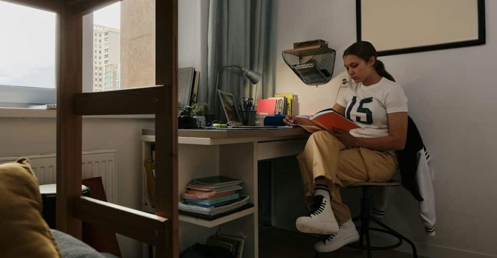 A young girl sitting at a desk in a room, studying a book.