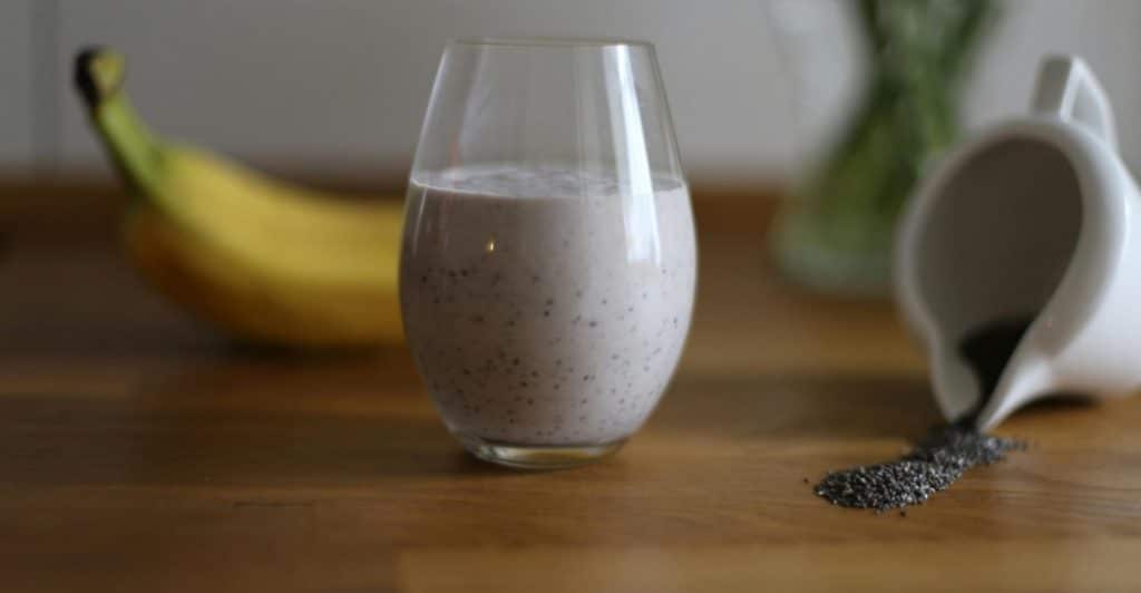 A clear glass containing chia fresca, next to a banana and scattered chia seeds on a wooden table.