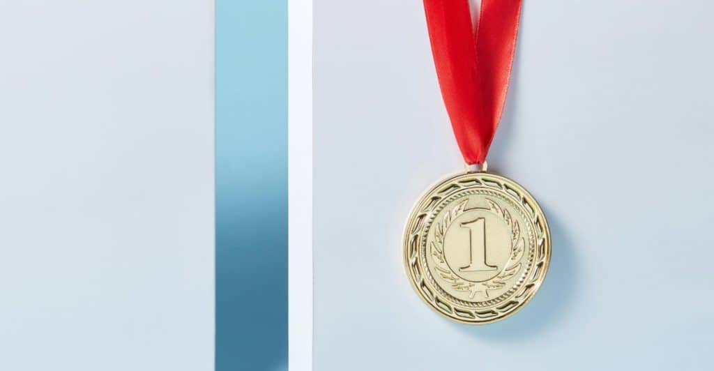 A gold medal with a red ribbon is displayed against a background with blue and white sections.