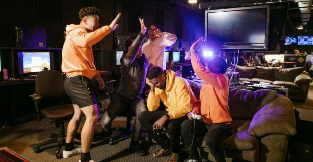 A group of people wearing matching hoodies celebrating together in an indoor space with gaming consoles.