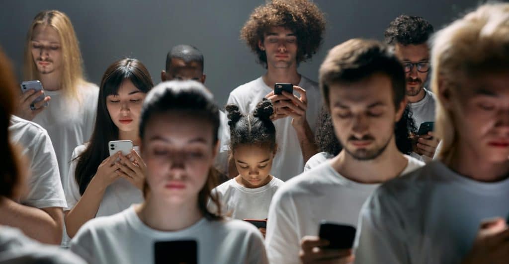 A group of people standing close together, looking down at their smartphones.