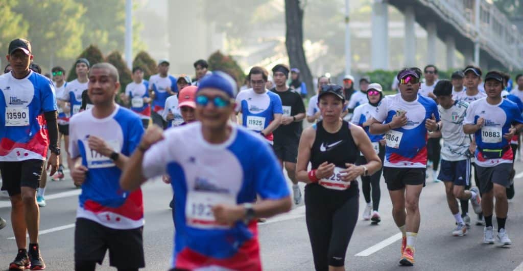 A large group of people wearing athletic attire running together on a paved road.