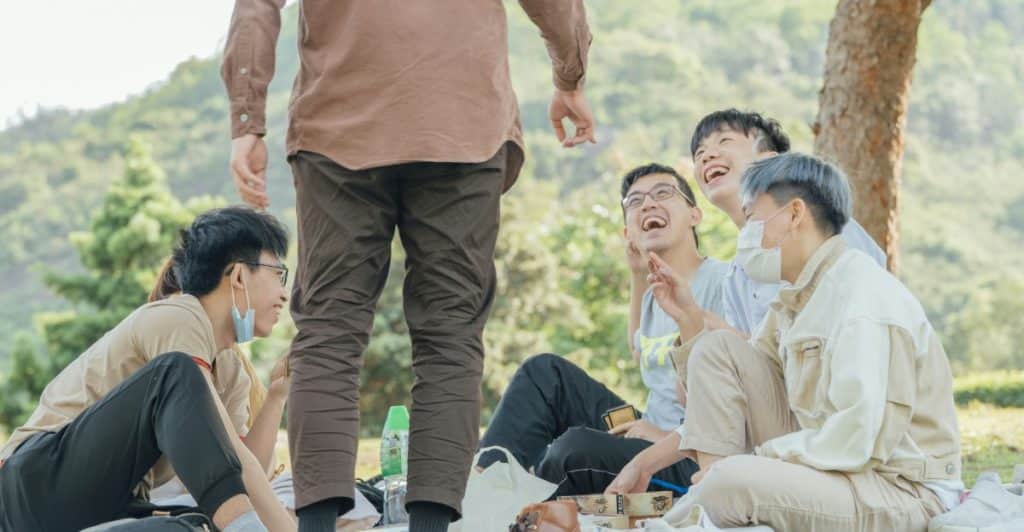 A group of several people are sitting and talking on a grassy area outdoors.