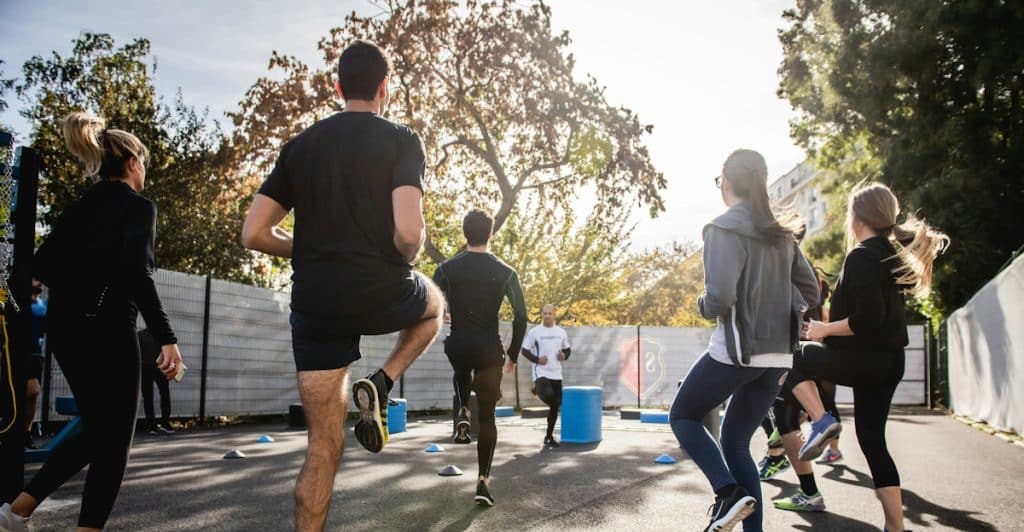 A group of people in athletic wear performing dynamic stretches outdoors on an asphalt surface.