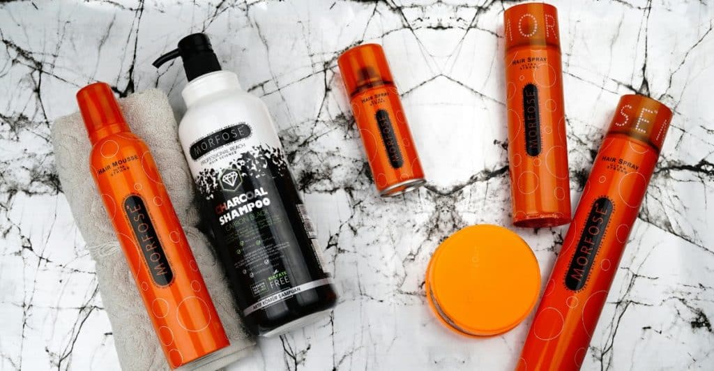 Several orange and black bottles of hair products are arranged on a marble surface.