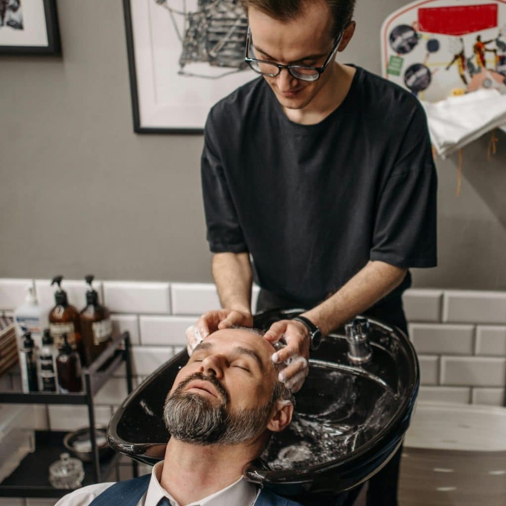 A man is getting his hair washed in a salon sink by a barber.