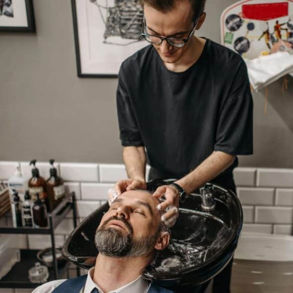 A man is getting his hair washed in a salon sink by a barber.