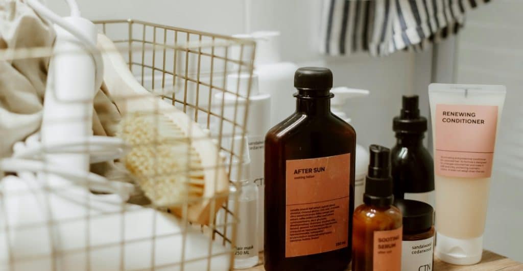 Assorted hair care products, including conditioner, after-sun lotion, and spray bottles, are arranged on a shelf next to a basket.
