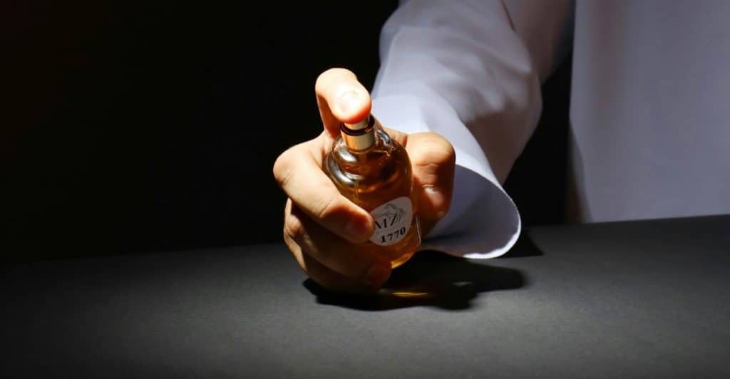 A hand holding a small bottle of fragrance and spraying it.