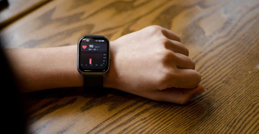 A person's wrist wearing a smartwatch displaying health data including heart rate, illustrating the concept of tracking health metrics.