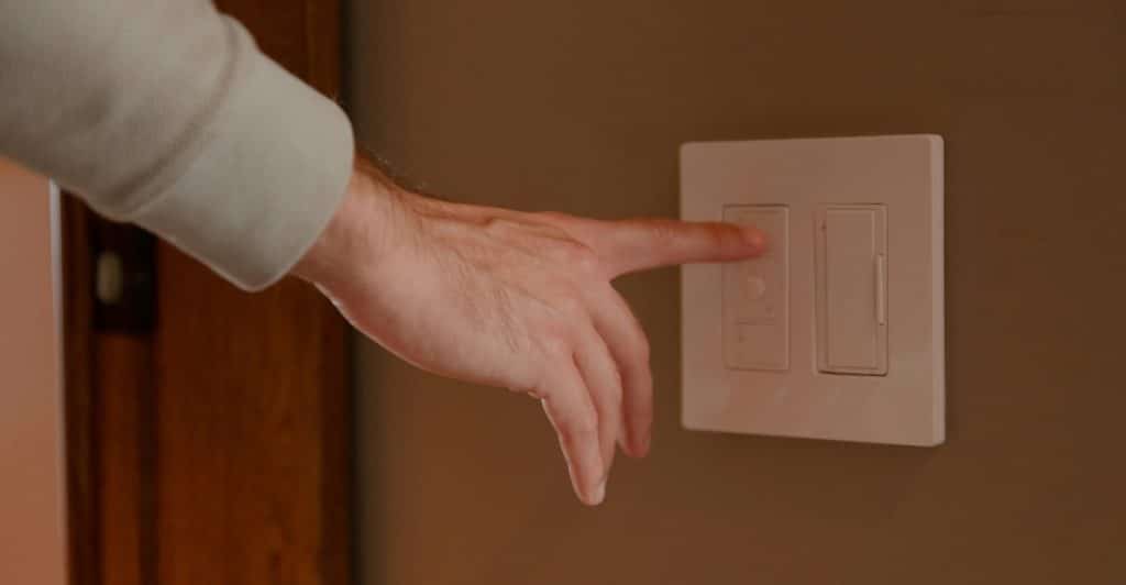 A hand adjusting a dimmer light switch on a wall.