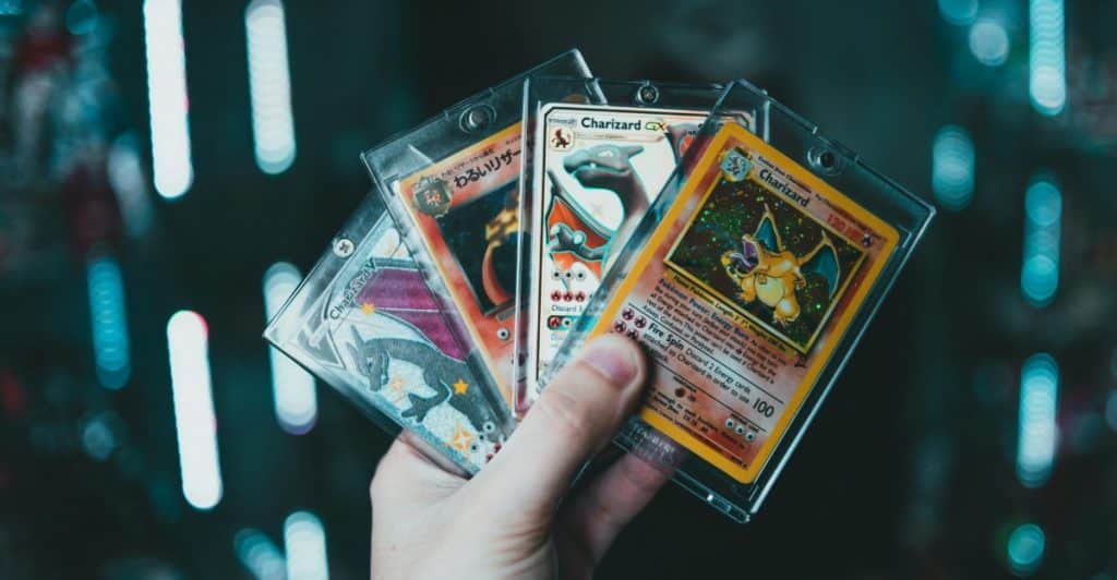  A hand holding several trading cards in protective sleeves, with a blurred background of lights.
