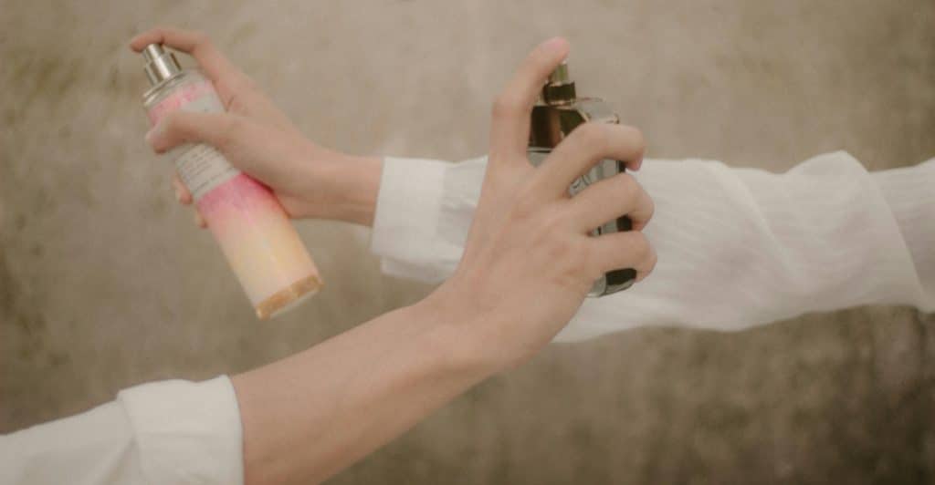 Two hands are spraying different bottles of fragrance.