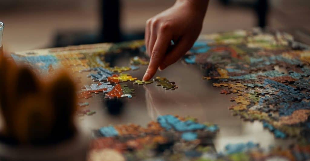 Close-up of hands placing pieces in a colorful jigsaw puzzle on a table.