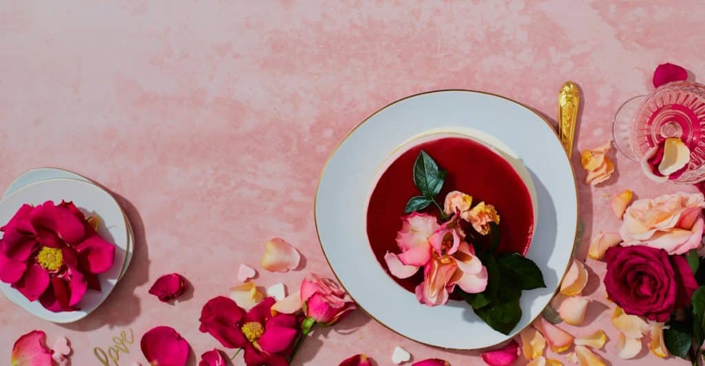 Pink floral arrangement and a glass of red hibiscus tea on a pink background.