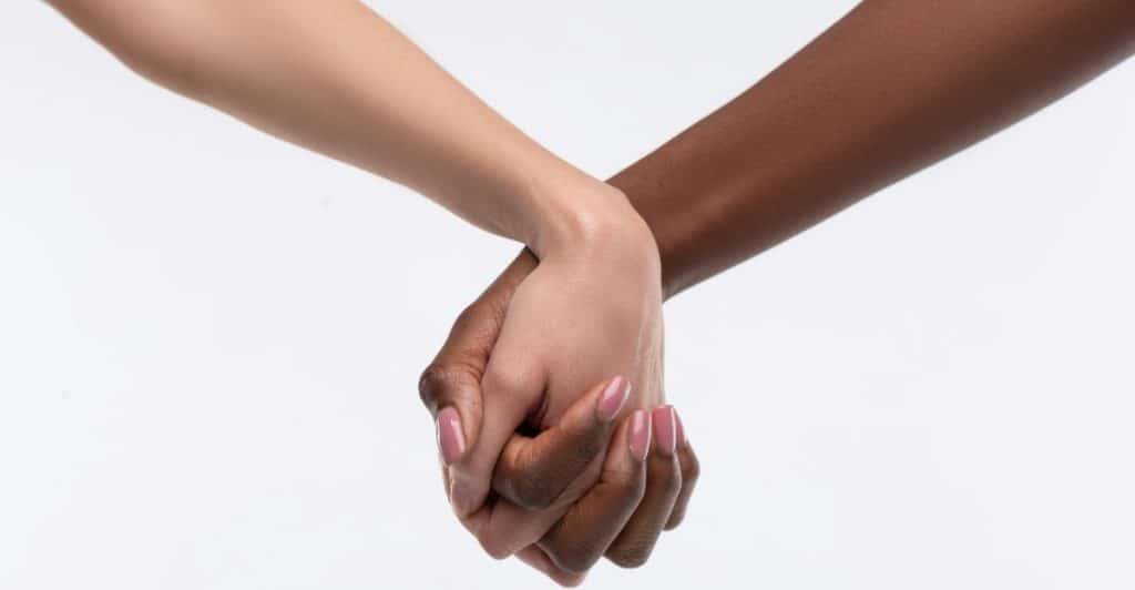 Two people with different skin tones are holding hands against a white background.