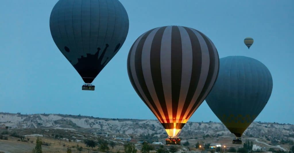 Several hot air balloons flying over a landscape at dusk.