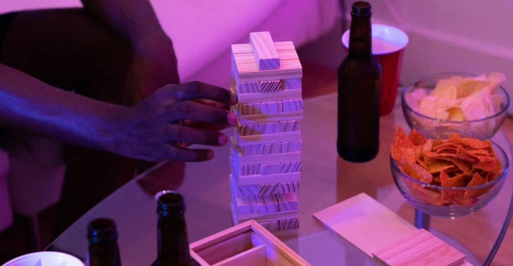  A Jenga tower, snacks, and drinks on a glass table, with a person's hand visible.