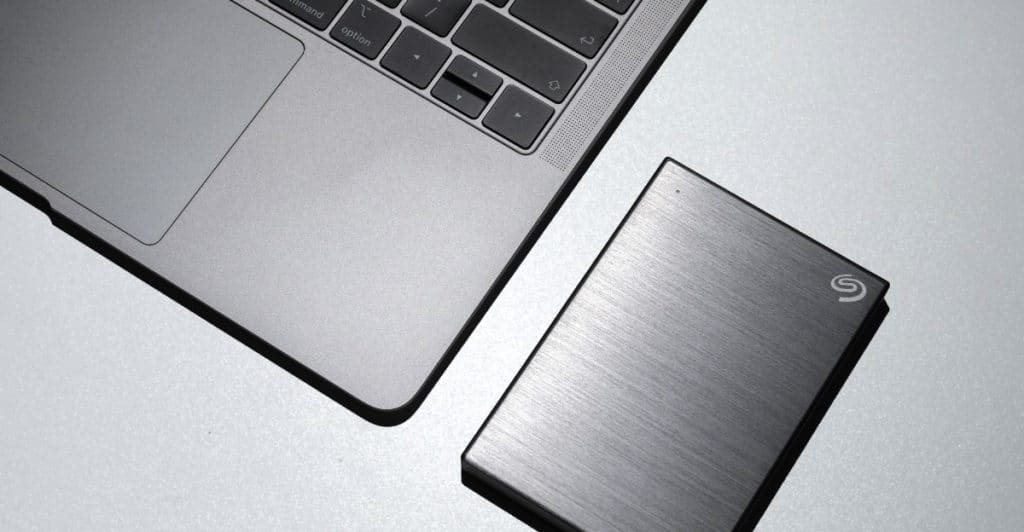 A laptop next to a silver external hard drive on a light-colored surface.