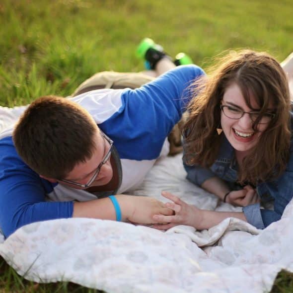 A man and a woman laughing and lying on a blanket in the grass.
