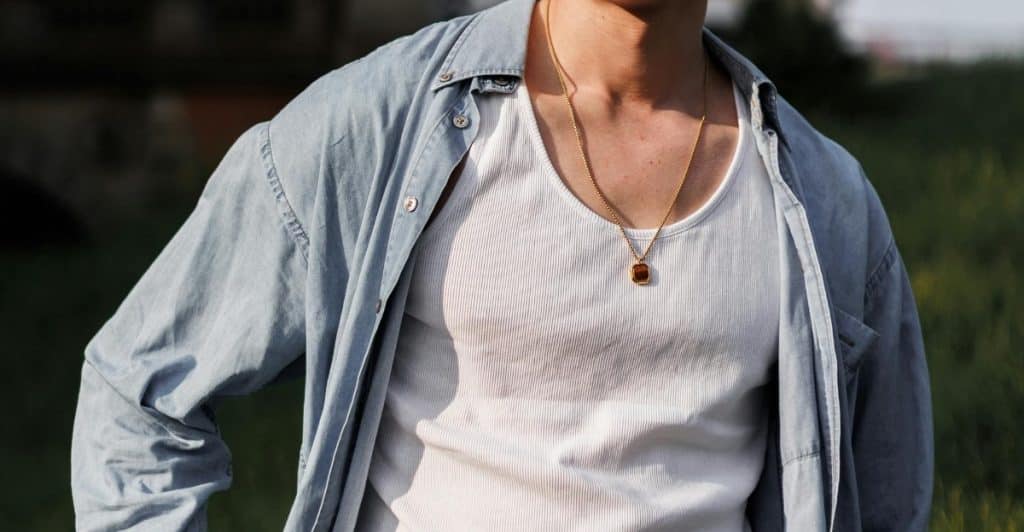  Close-up of a person wearing a white tank top and an unbuttoned blue shirt with a gold necklace.