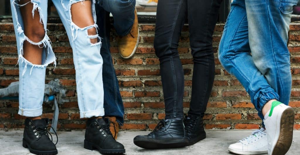 The lower legs and feet of four people wearing different styles of jeans and shoes.