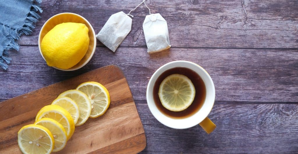 Lemon slices, tea bags, and a cup of tea with a lemon slice on a wooden table.