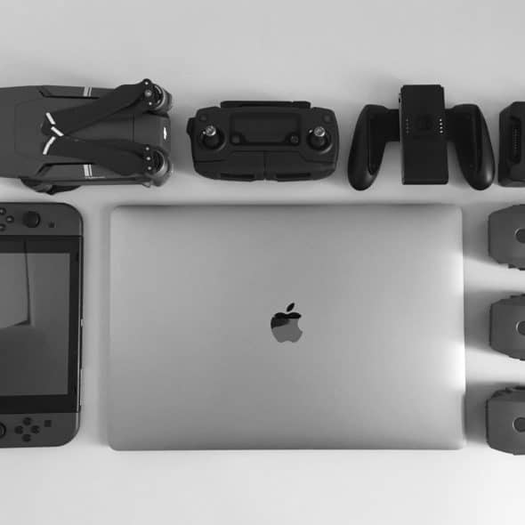 Overhead view of various electronic gadgets including a drone, controller, battery charger, batteries, a Nintendo Switch, and an Apple MacBook laptop.