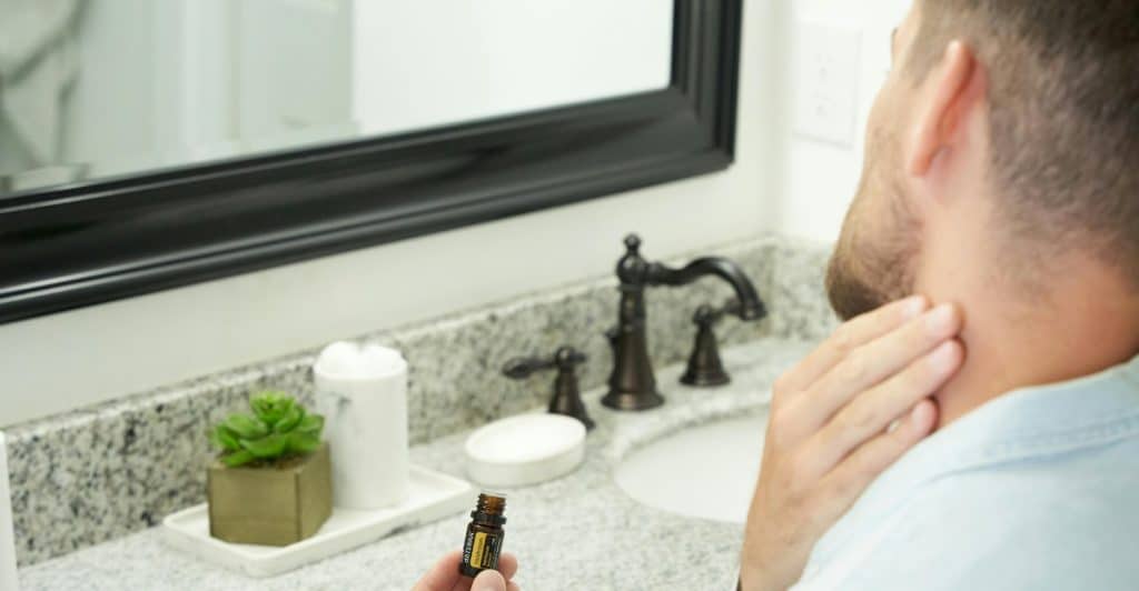 A man applying fragrance to his neck in a bathroom.