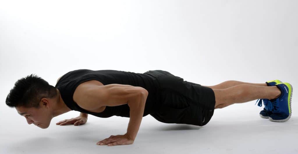 A man wearing a black tank top doing a push-up with a white background.